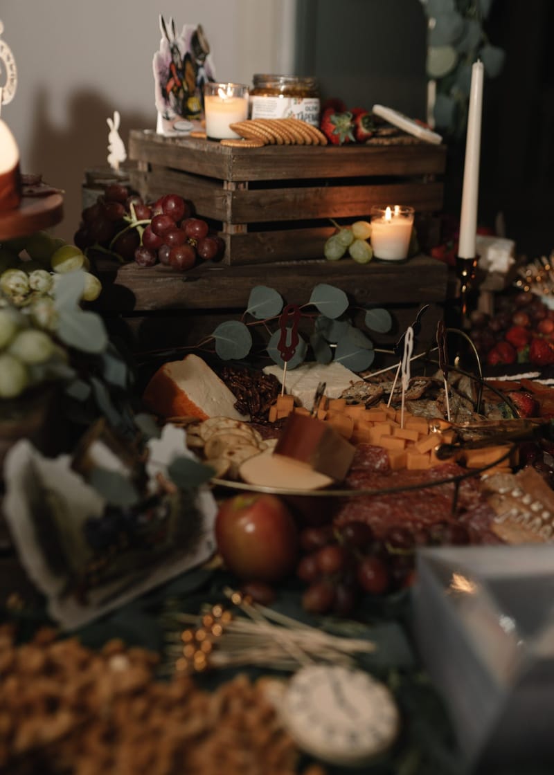 Grazing table with cheese, grapes and crackers on wooden crates with candles and an Alice cutout