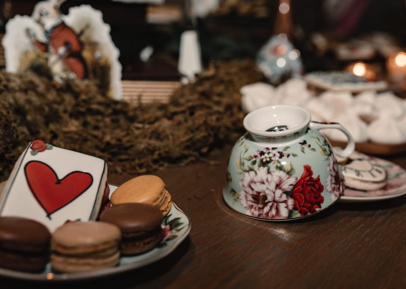 Macarons, a heart playing card cookie and a tipped floral teacup on a wooden table