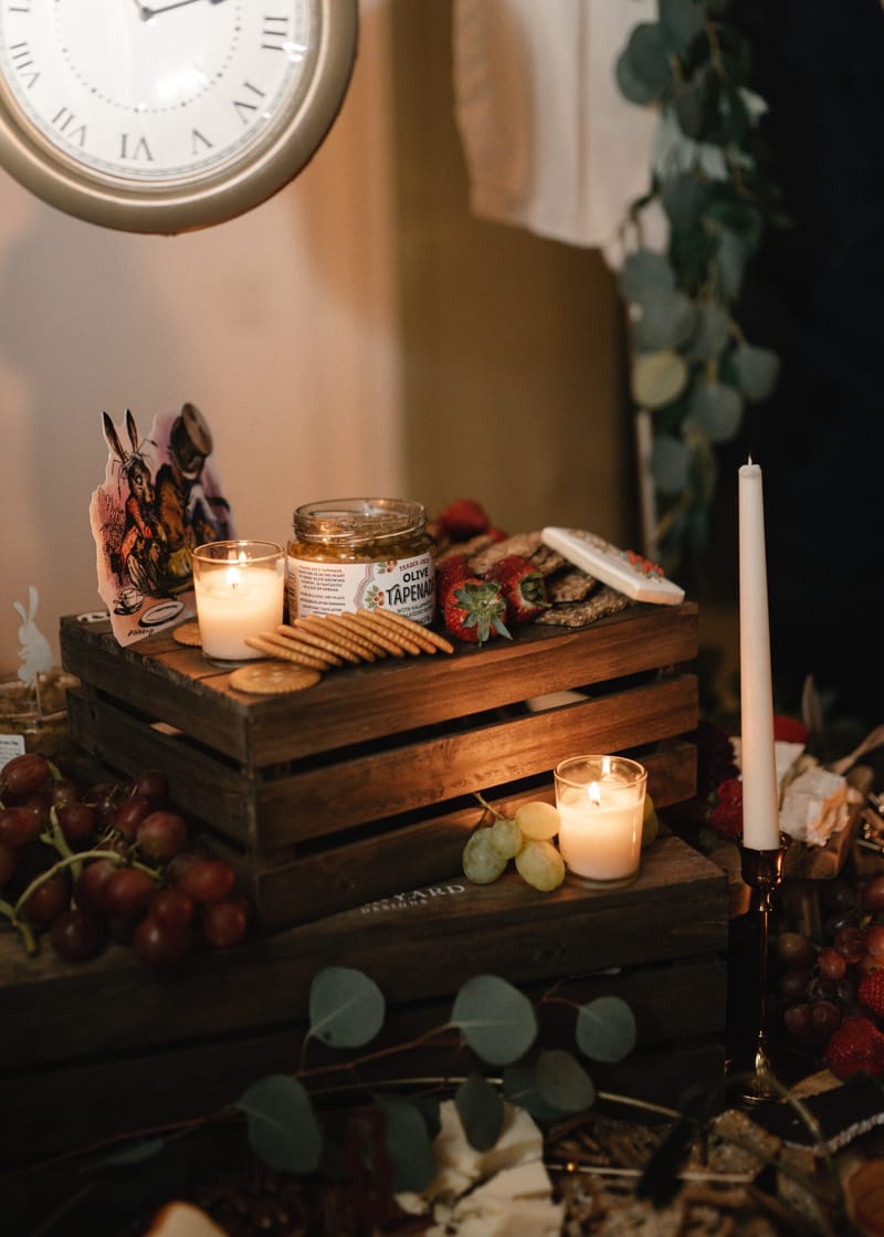 Wooden crate of crackers, a jar and candles under a large wall clock with eucalyptus