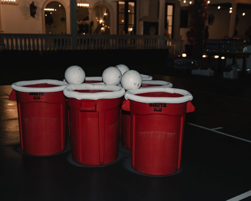 Giant pong game of red bins topped with white balls on a black table