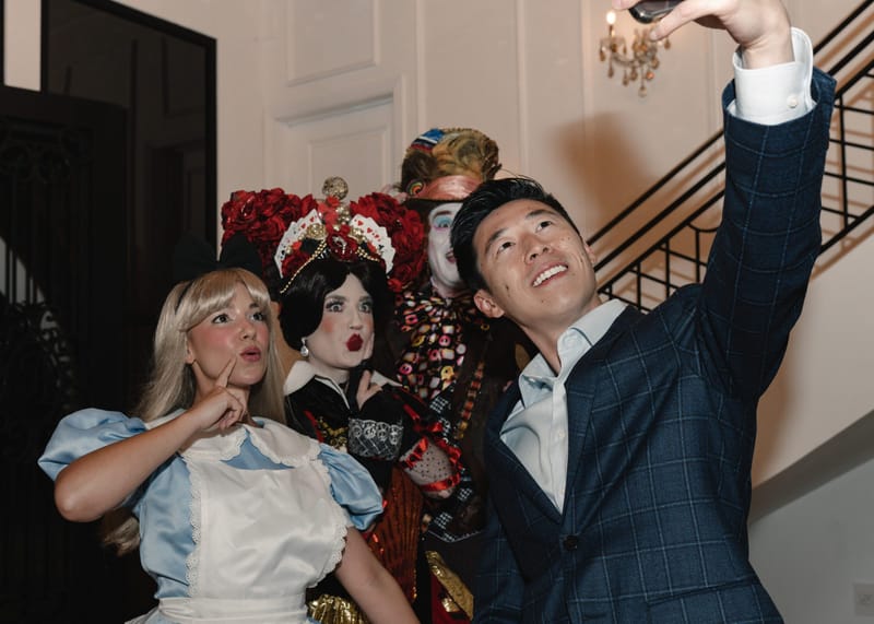 A guest in a checked blazer taking a selfie with Alice, the Queen of Hearts and the Mad Hatter