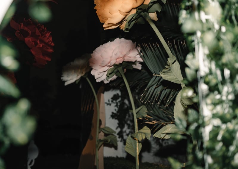 Oversized pink and red paper flowers among palm leaves and greenery