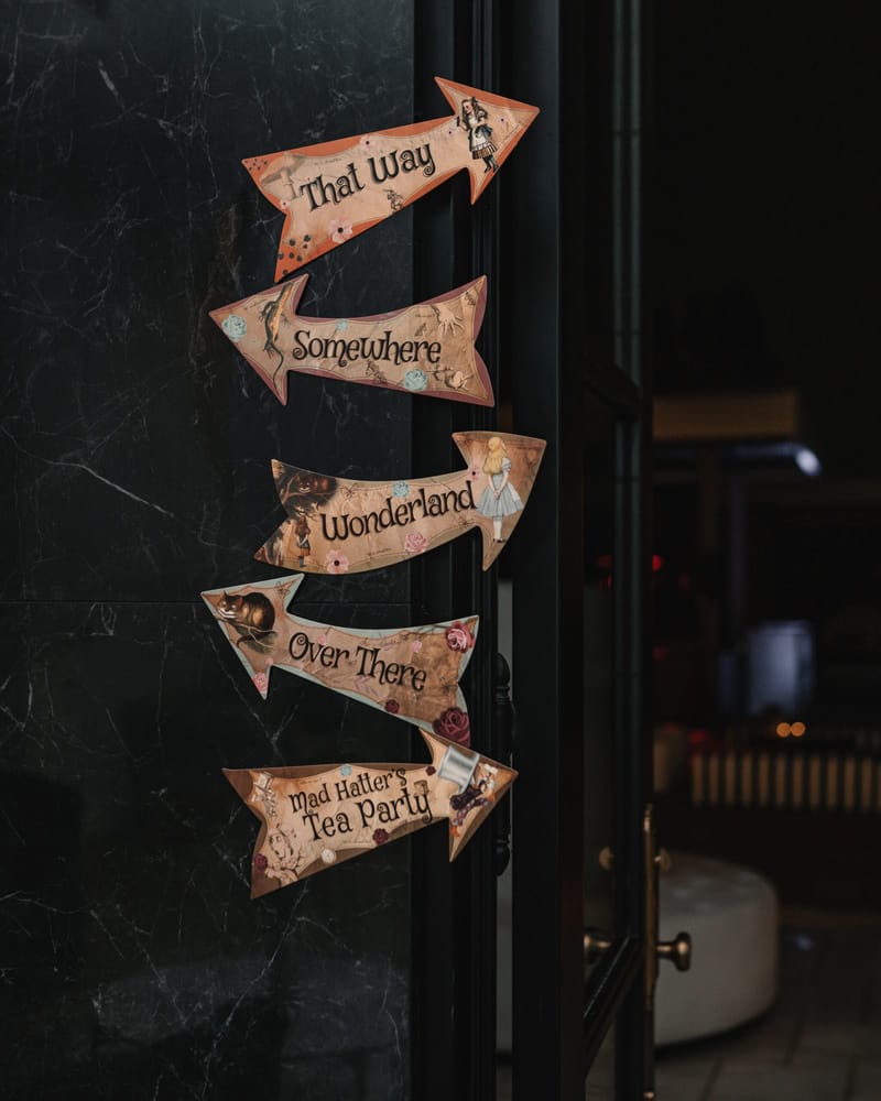 Stack of arrow signs reading That Way, Somewhere, Wonderland, Over There and Mad Hatter’s Tea Party