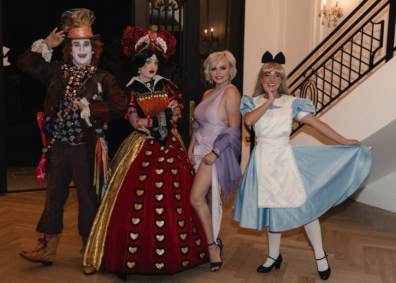 The Mad Hatter, the Queen of Hearts, a guest in a lavender gown and Alice by the stairs