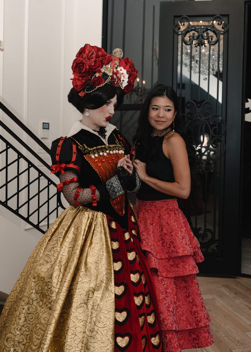 The Queen of Hearts posing with a guest in a red tiered skirt near a staircase