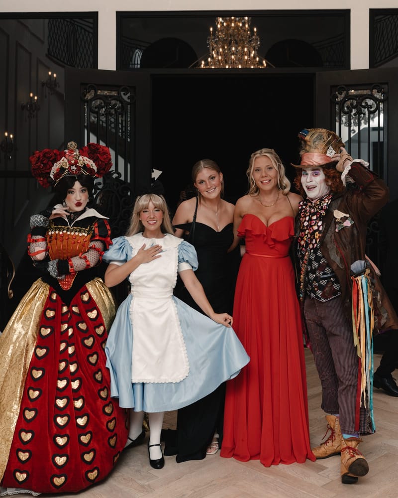 The Queen of Hearts, Alice, two guests in black and red gowns and the Mad Hatter in a doorway