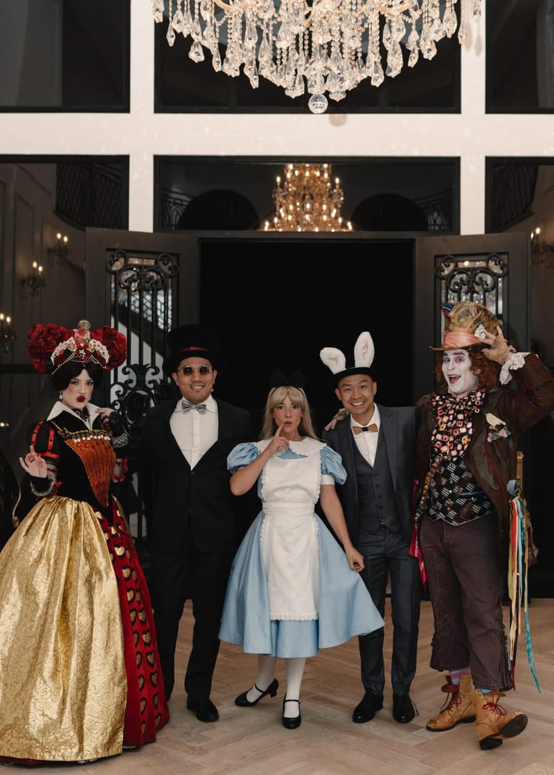 Guests in a tuxedo and in white rabbit ears posing with the Queen of Hearts, Alice and the Mad Hatter