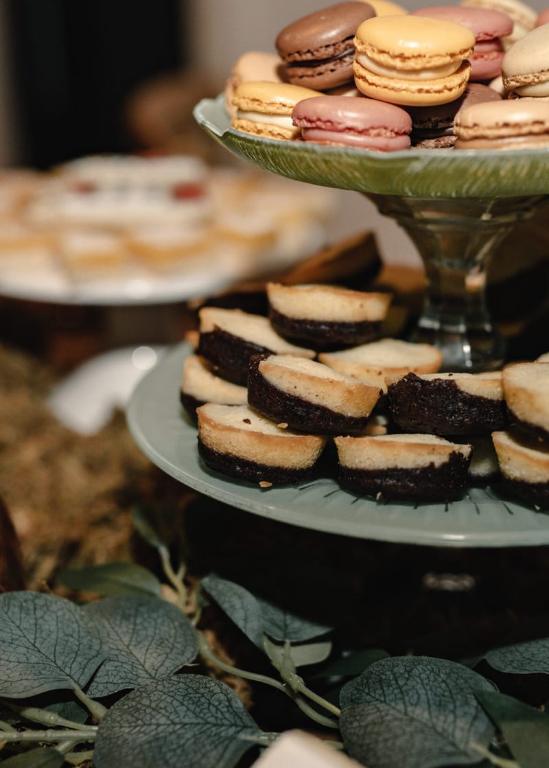 Macarons and chocolate cake bites on green glass cake stands with leaves