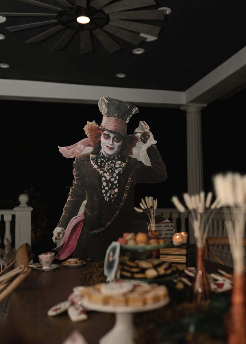 Life-size Mad Hatter cutout behind a dessert table with pampas grass and teacups