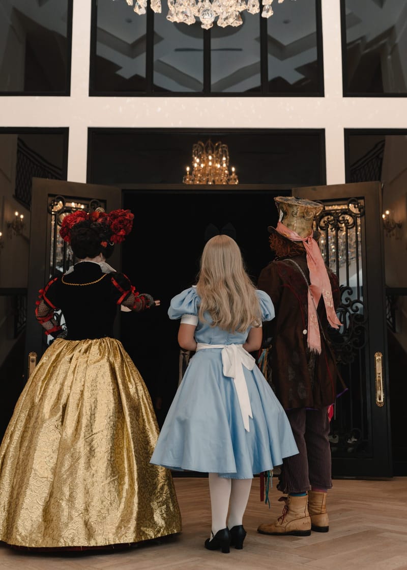 The Queen of Hearts, Alice and the Mad Hatter seen from behind, walking toward iron doors