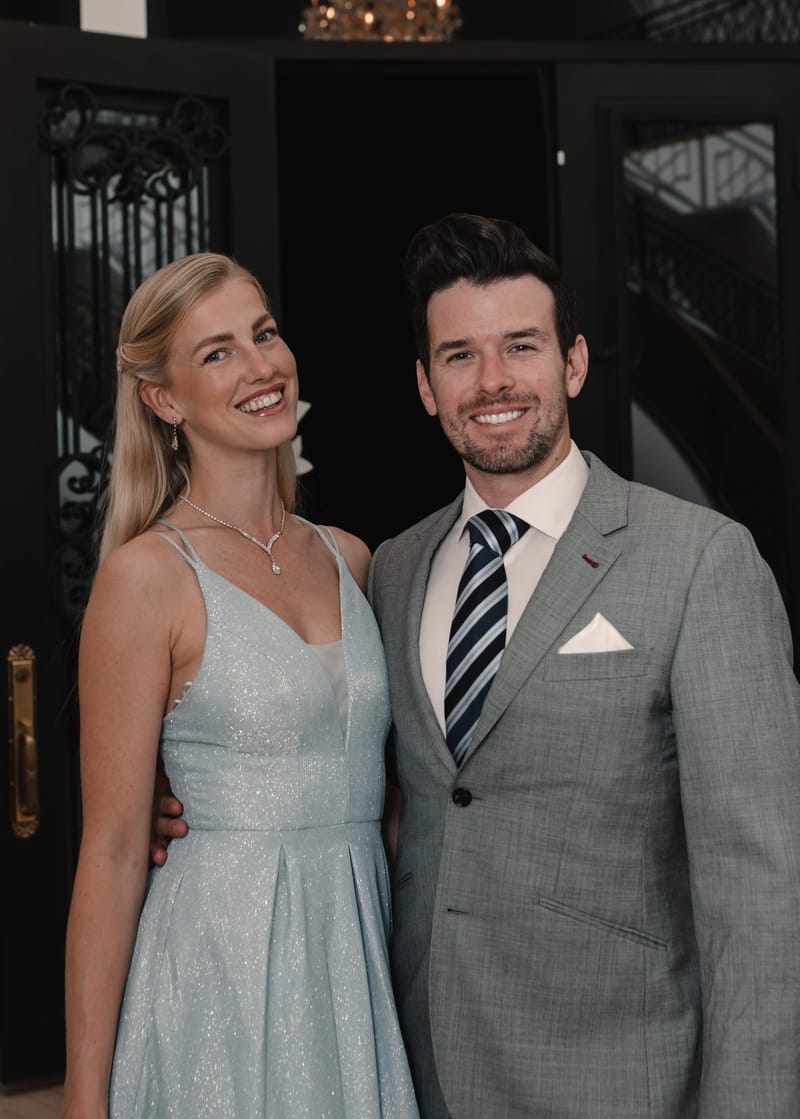 A guest in a pale blue dress and a guest in a grey suit posing together