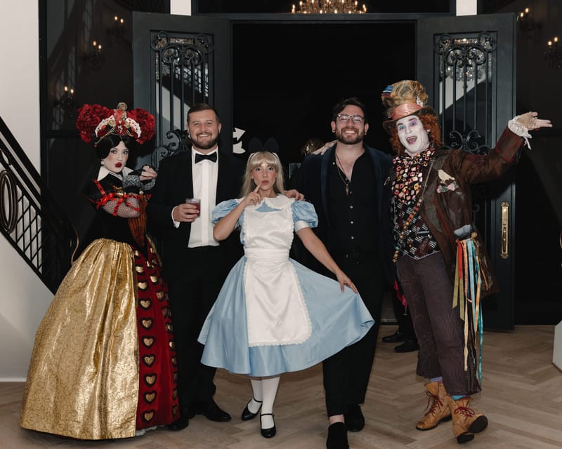 The Queen of Hearts, two guests in black, Alice and the Mad Hatter posing in a doorway
