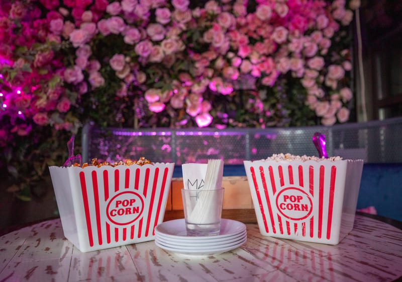 Red and white striped popcorn boxes and a stack of plates in front of a wall of pink roses