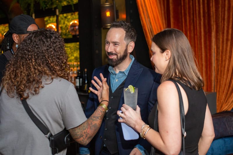 Guests talking with drinks in hand in front of rust velvet curtains