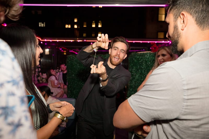A man in black stretching a length of string between his hands as guests watch on the rooftop