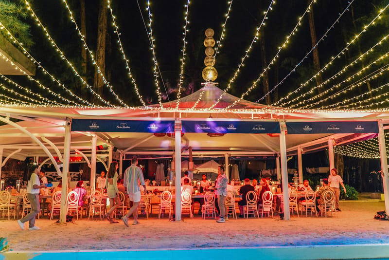 Guests dining in a white tent on the sand under fairy lights radiating overhead