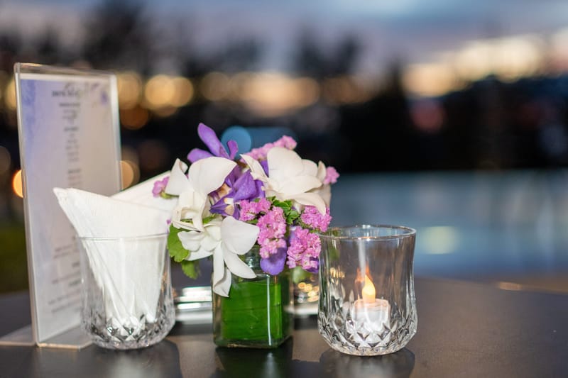 Table with an orchid arrangement, a candle holder and a menu stand at dusk by the water