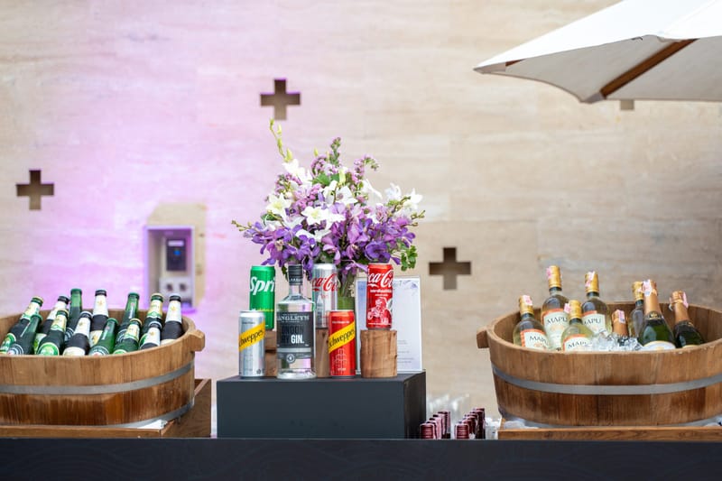 Drinks station with wooden tubs of beer and wine bottles, canned mixers and purple orchids