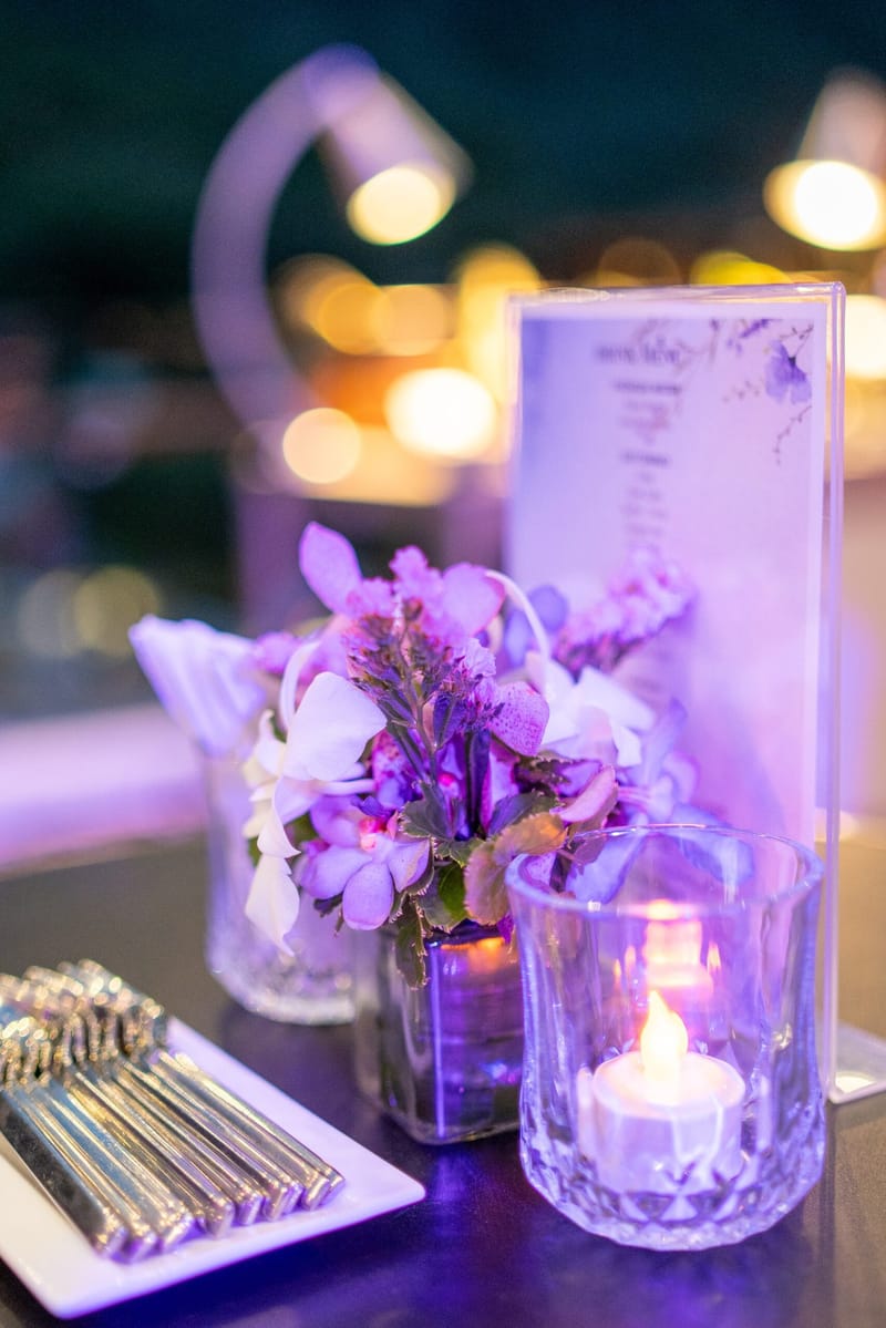 Purple-lit table with orchids, a candle, cutlery and a menu