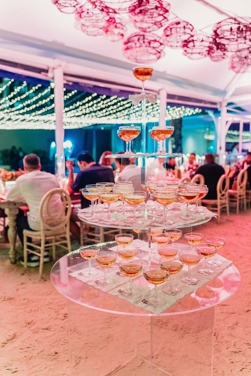 Tiered acrylic champagne coupe tower under pink wicker lanterns inside the dinner tent