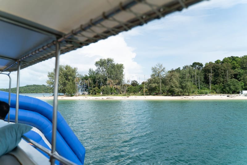 View from a boat's shaded deck with a blue slide toward an island beach