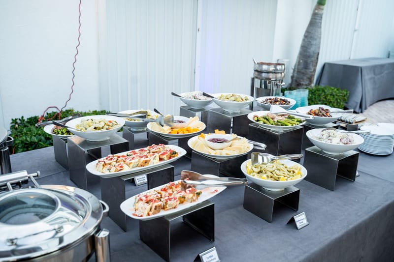Buffet of salads and plated dishes on raised black stands over a gray tablecloth