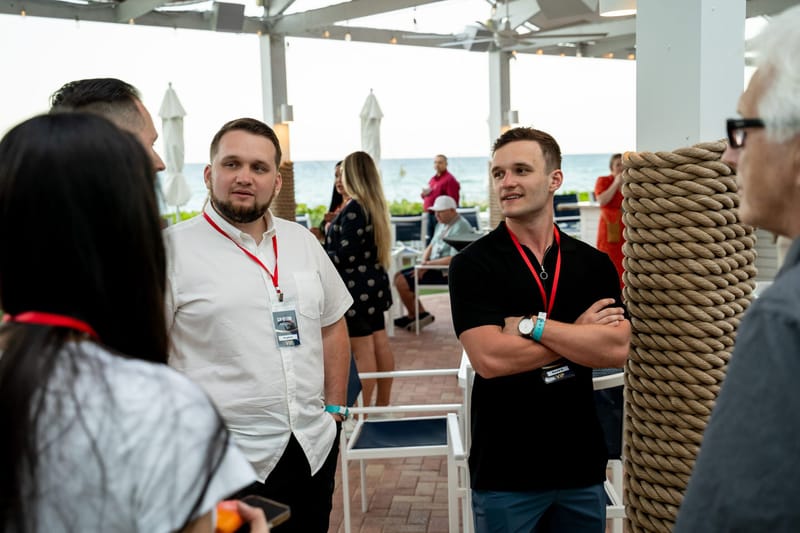 Guests in red lanyards talking on a covered terrace with the ocean behind