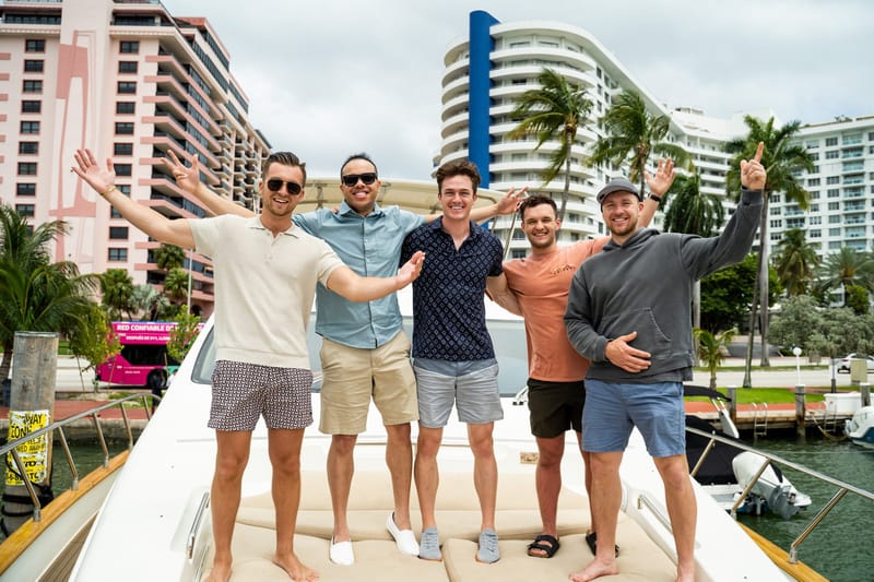 Five guests posing on a yacht deck with high-rise buildings and palm trees behind