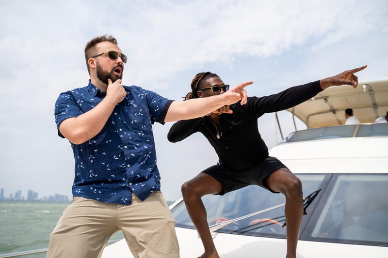 Two guests striking a pointing pose on a yacht deck with a city skyline in the distance