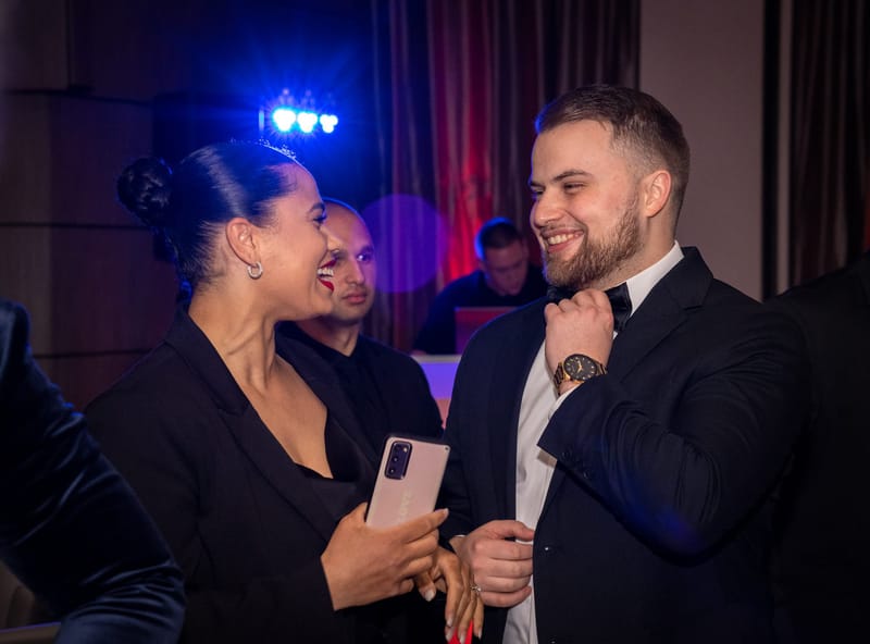 Two guests in evening wear laughing together under blue stage lights