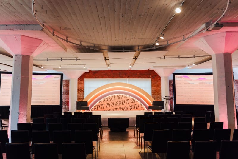 Main room with rows of black chairs facing an arch-shaped rainbow Connect backdrop between two agenda screens