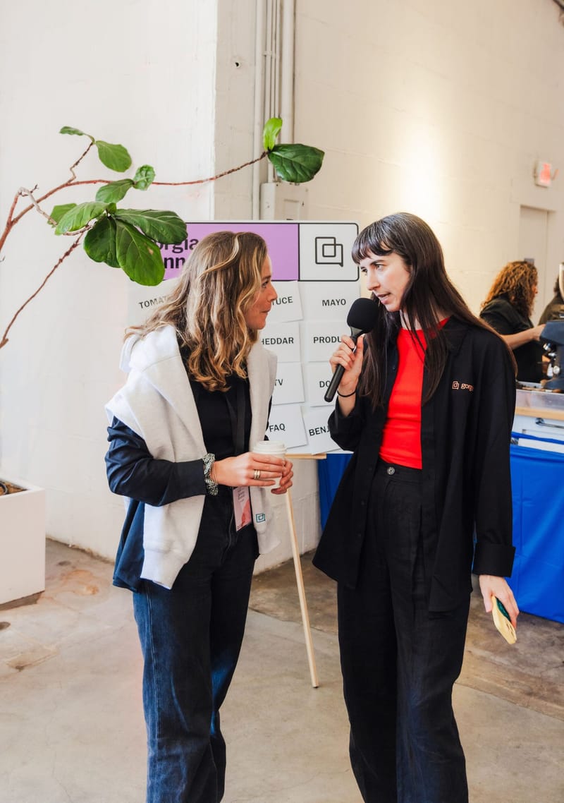 Two women talking with a microphone beside a Gorgias board of word cards reading Tomato, Mayo and Cheddar
