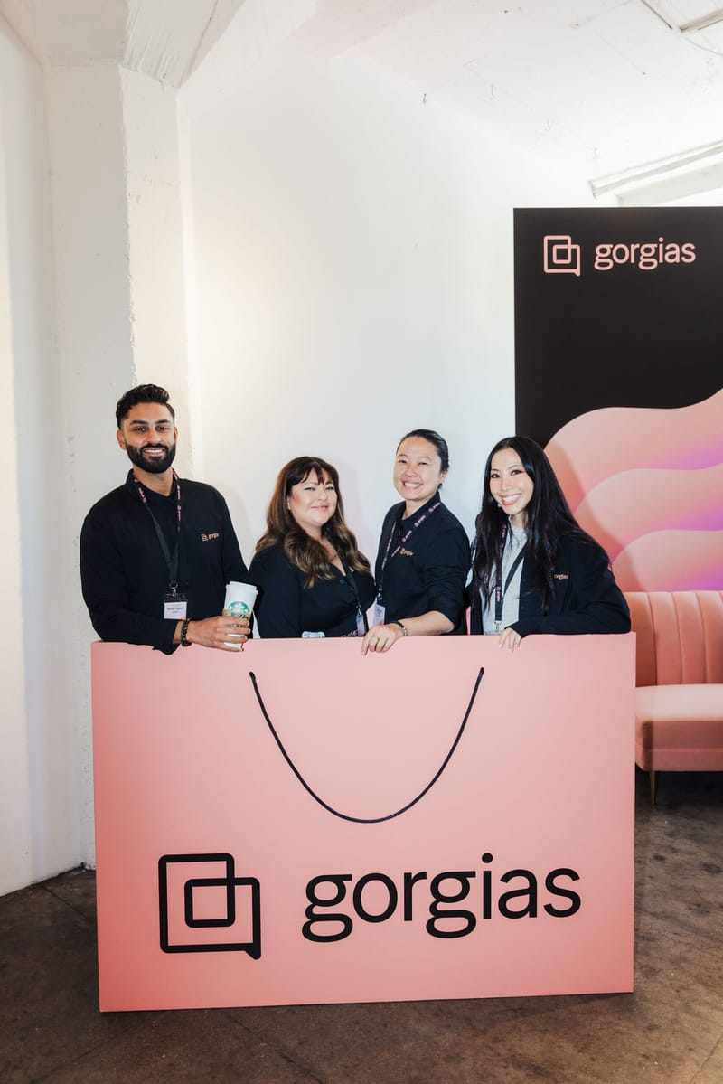 Four staff members behind a pink counter shaped like a shopping bag and printed with Gorgias