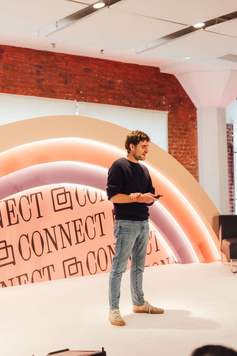 A man standing on stage in front of the rainbow Connect backdrop