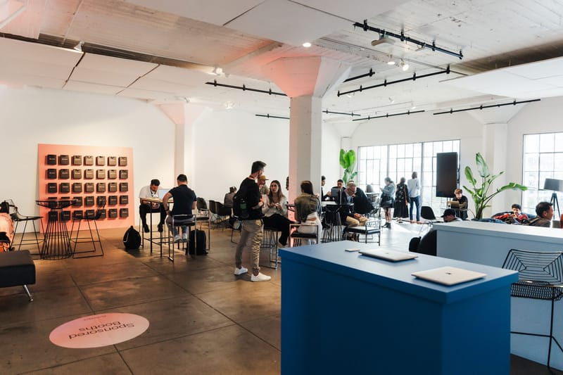 Open hall with a blue counter, a wall of bags and a floor decal reading Sponsored Booths