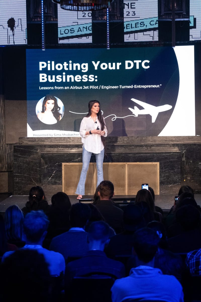 Speaker presenting Piloting Your DTC Business under LED panels reading Los Angeles, CA