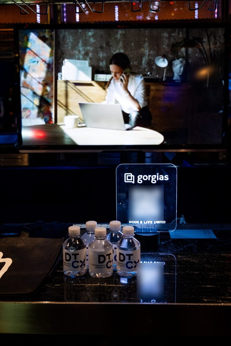 Lit Gorgias Book a LIVE Demo QR sign behind DTCx Ecommerce Growth water bottles on a bar