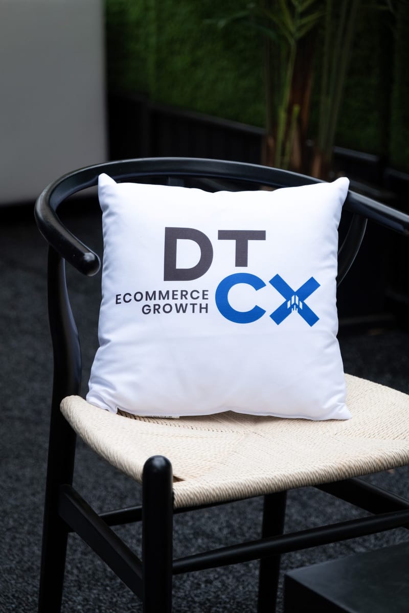 White pillow printed DT CX Ecommerce Growth on a black wishbone chair
