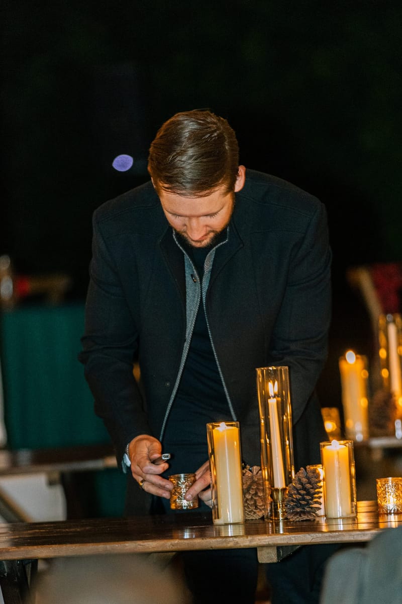 A guest adjusting a candle on a wooden table set with tall pillar candles and a pinecone