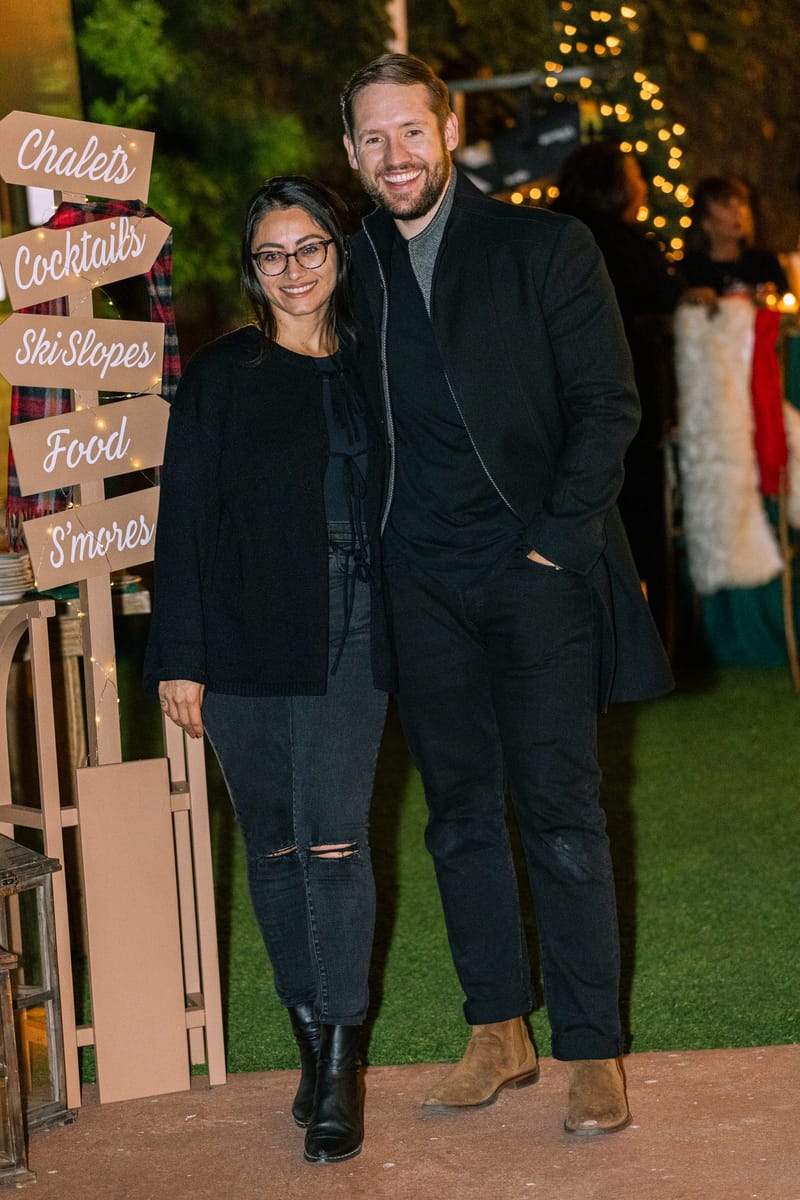 Two guests smiling beside a wooden signpost pointing to Chalets, Cocktails, Ski Slopes, Food and S'mores
