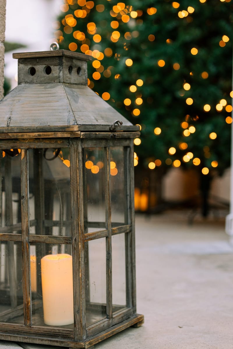 Wooden lantern with a pillar candle in front of a Christmas tree strung with lights
