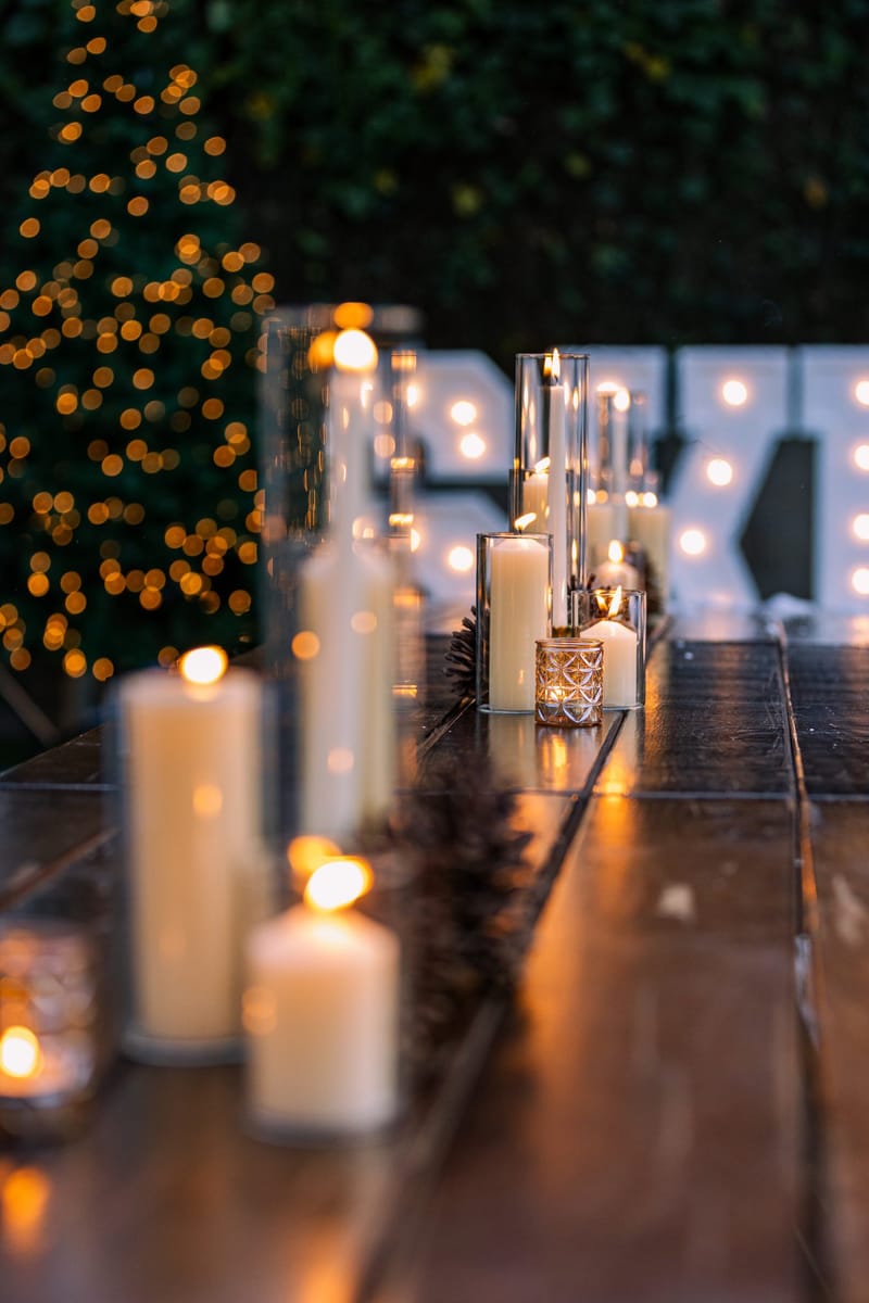 Pillar candles in glass along a dark wooden table, with lit SKI letters behind