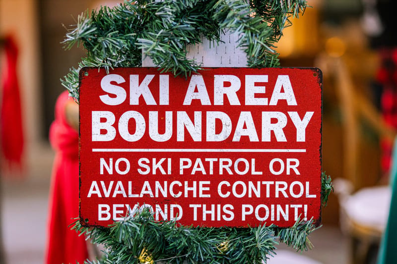 Red Ski Area Boundary sign reading No Ski Patrol or Avalanche Control Beyond This Point, wrapped in garland