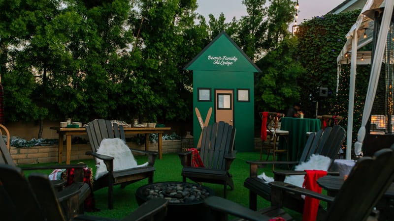 Garden with a green Dennis Family Ski Lodge cabin, Adirondack chairs and a fire pit