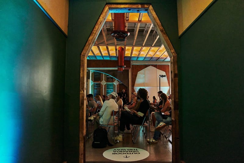 Seated audience seen through an angled doorway, with an Outdoor Veranda This Way floor decal