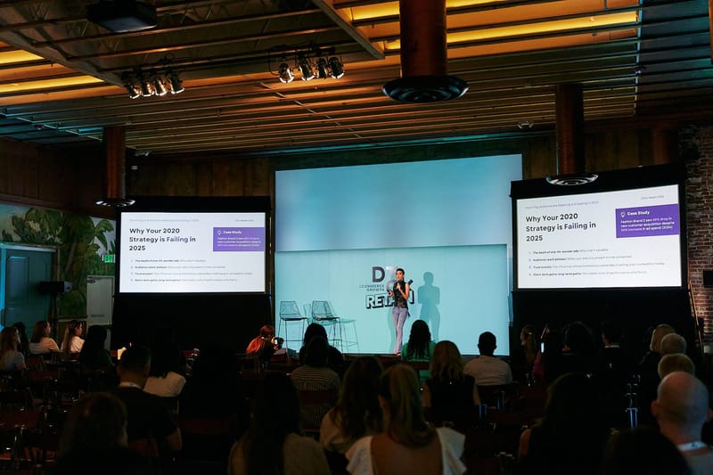 A speaker on the DTCx Retain stage between screens reading Why Your 2020 Strategy is Failing in 2025