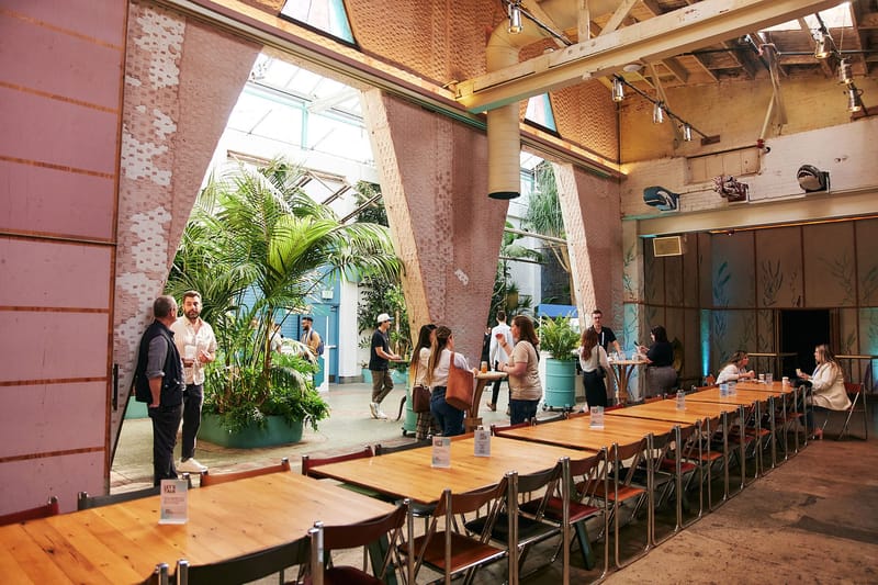 Long wooden tables in a hall with angled walls opening onto a planted courtyard