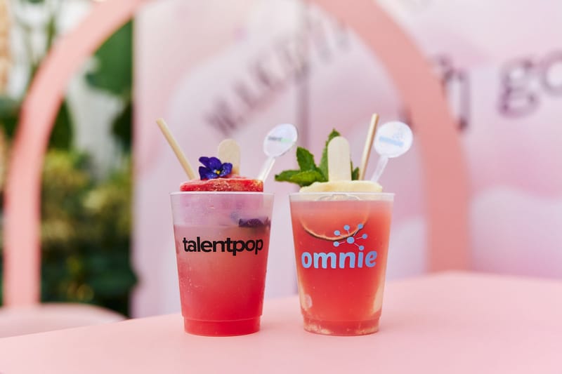 Two garnished drinks in cups printed talentpop and omnie, with the pink Gorgias backdrop behind