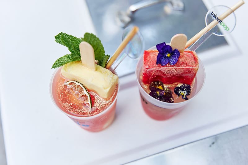 Two drinks topped with ice pops, mint and edible flowers, one cup printed talentpop
