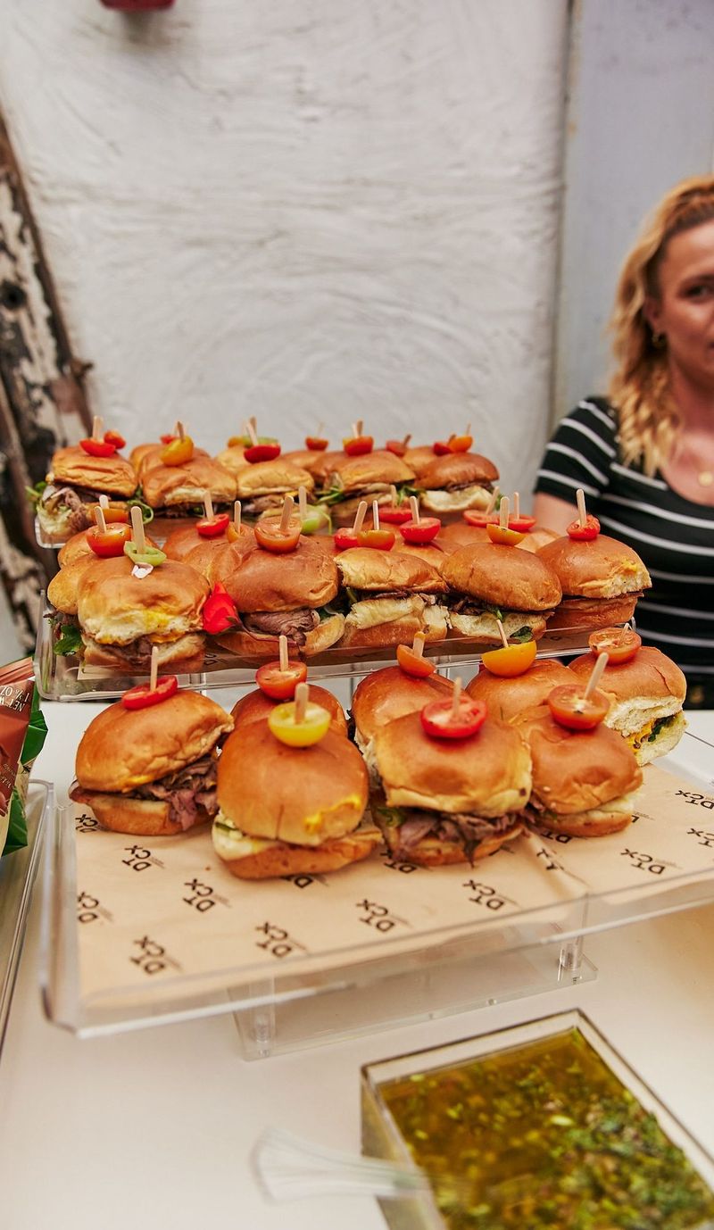 Tray of sliders with cherry tomato picks on branded paper
